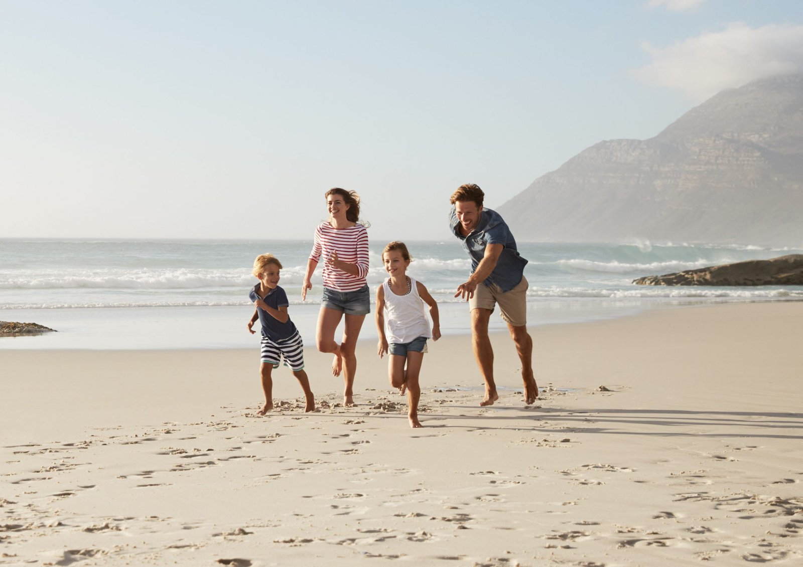 Parents Running Along Beach With Children On Summer Vacation